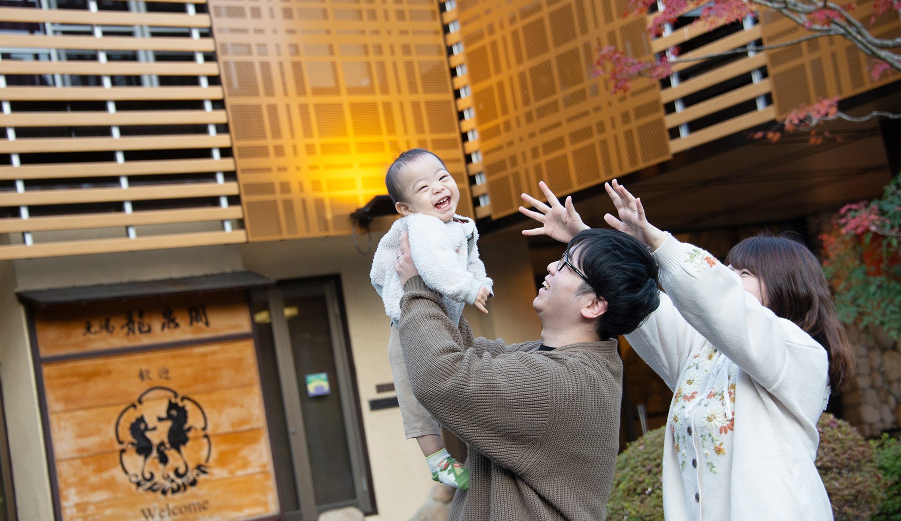 元湯龍泉閣 — 神戸・有馬温泉 · 紅葉の玄関先で子どもを抱き上げる家族連れ、赤ちゃん歓迎の宿
