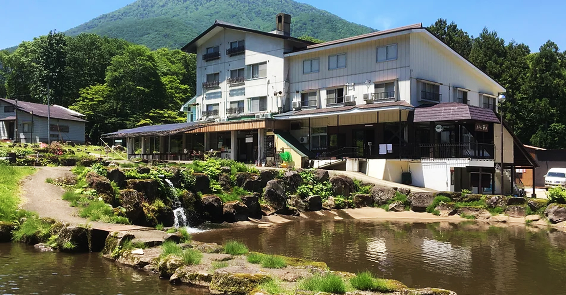 ホテル若月 — 長野県信濃町・黒姫高原 · 黒姫山を背に建つ館と、手前に広がるイワナ・ニジマスの釣り堀