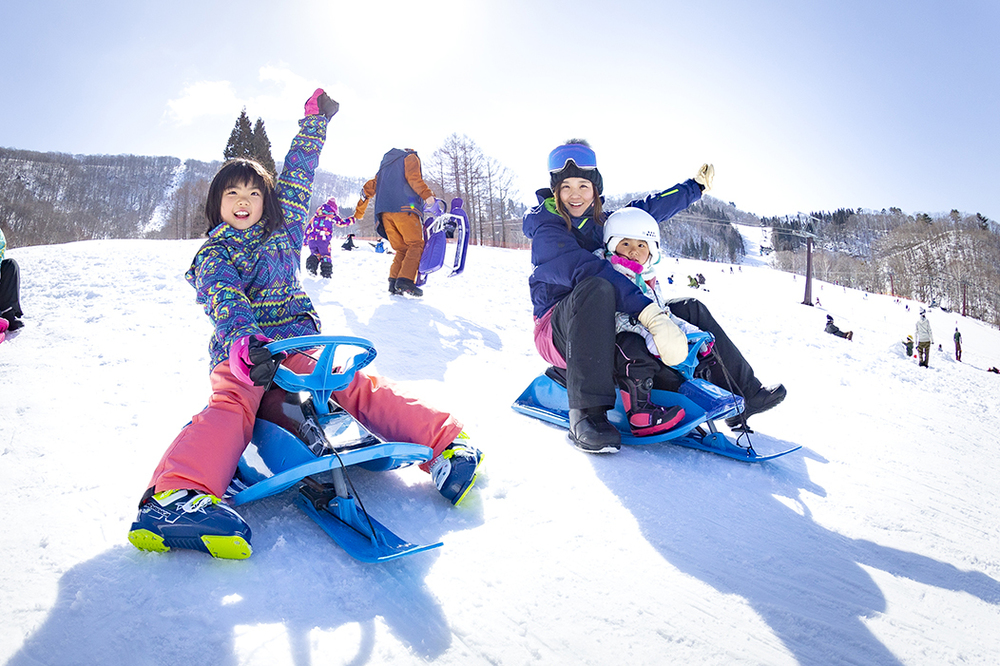 ホテルタングラム — 長野県信濃町・斑尾高原 · タングラムスキーサーカスのゲレンデでソリ遊びをする親子