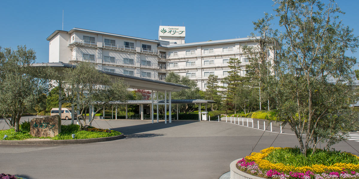 ガーデンホテルオリーブ — 三重県桑名市・長島温泉 · オリーブの木と花壇が並ぶ車寄せと客室棟