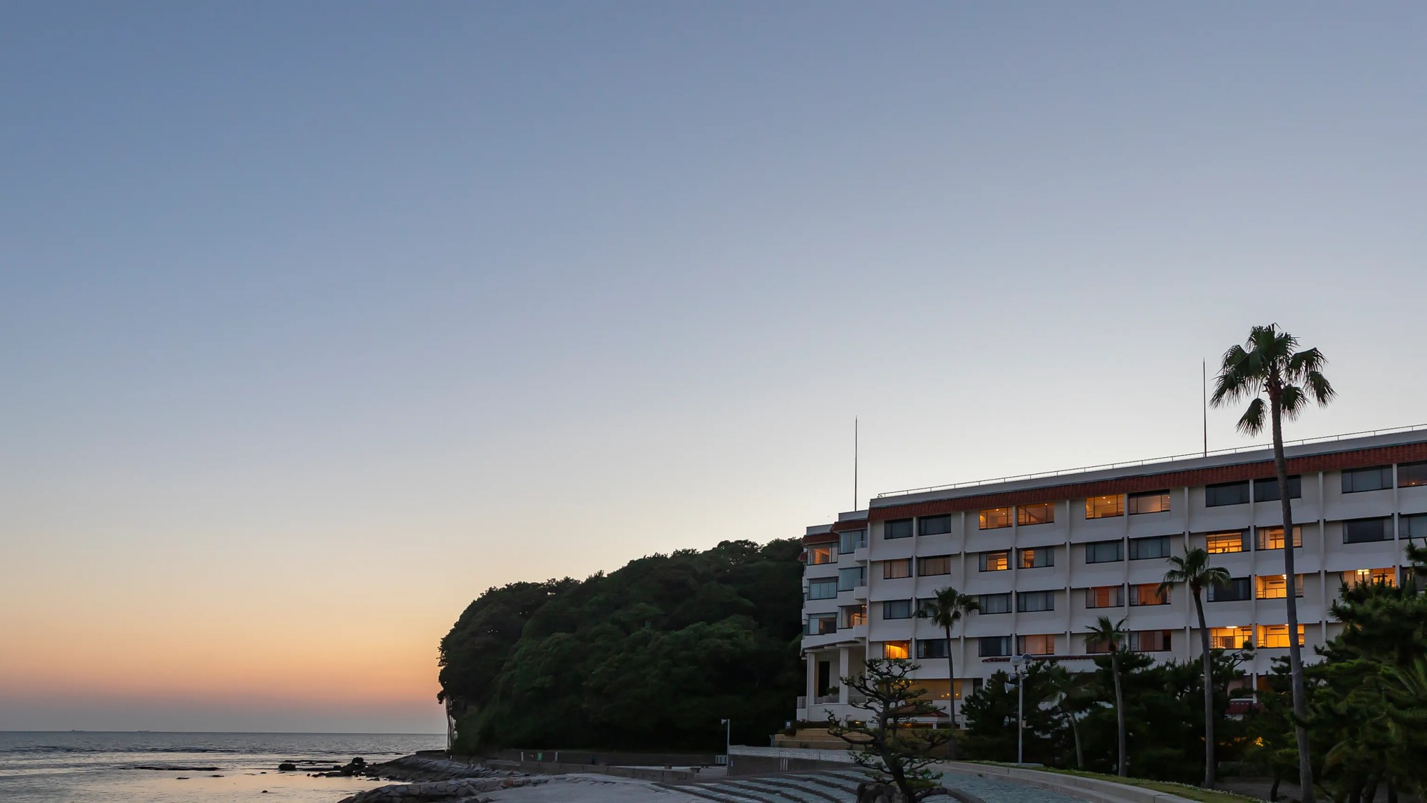 白良荘グランドホテル — 白浜町 · 夕暮れの海辺に建つホテルの外観とヤシの木