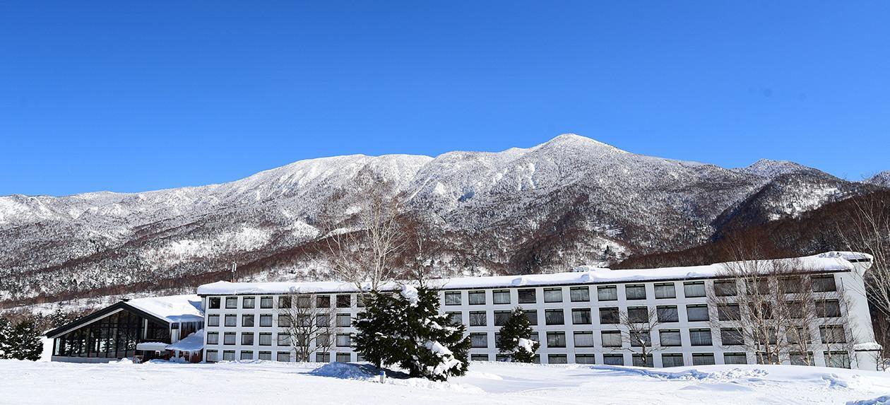 志賀高原プリンスホテル — 長野県山ノ内町 · 雪の焼額山を背にした低層のホテル棟と青空
